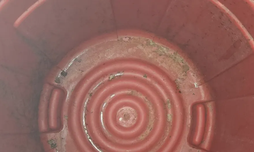 The inside of a large trash can before cleaning, with dried residue and debris stuck to the base.
