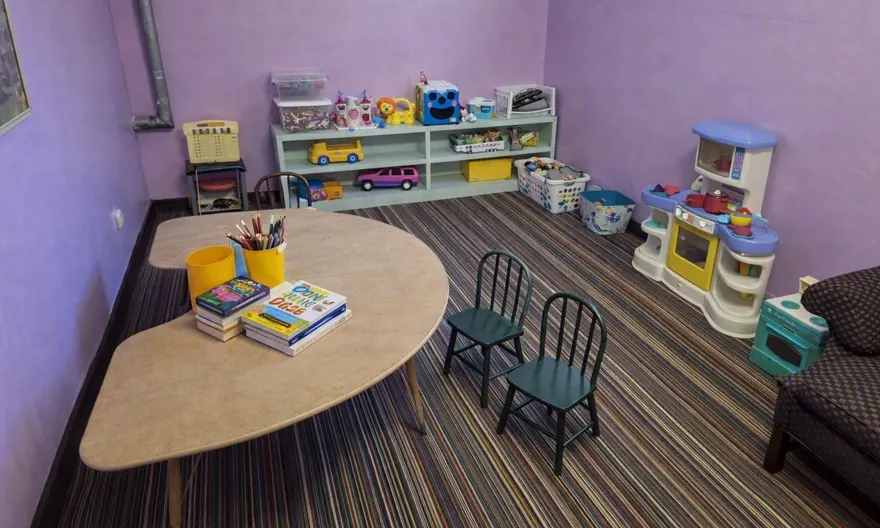 The same nursery after cleaning: toys shelved, table cleared, carpet vacuumed and chairs squared away.