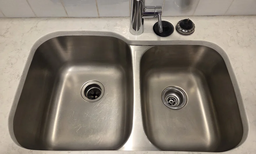 Clean stainless steel double kitchen sink with clear basins, drains and surrounding counter.